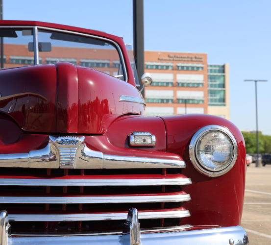 A close-up view of the front of a vintage red car with chrome details, parked in an outdoor lot.