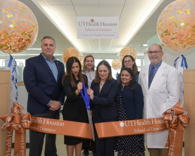 A group of dentists and administrative professionals cut a large ribbon.