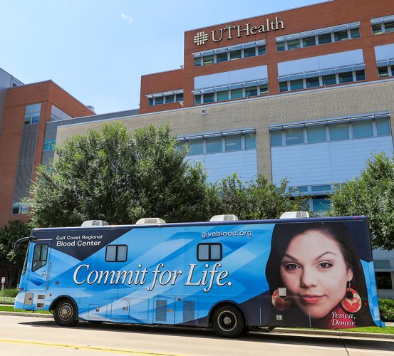 Blue coach bus sits parked in front of a building.