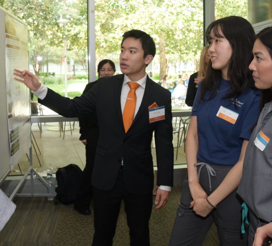 Suited man directs the attention of two women in professional attire towards his presentation.