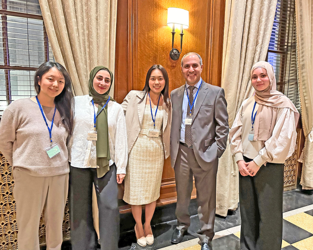 Group of five, four women and one man, stand shoulder to shoulder in professional attire wearing name badges.