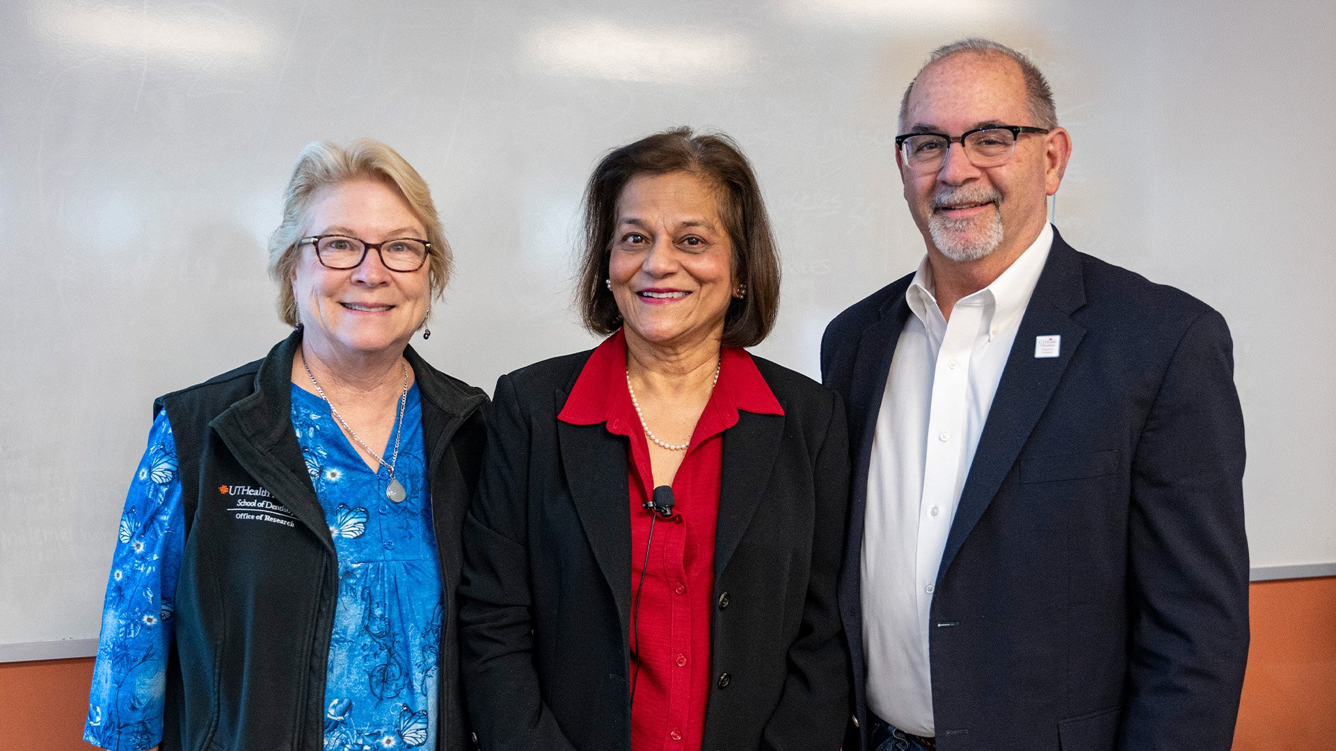 Three professionally-dressed adults stand side by side in front of a classroom whiteboard for a group photo.