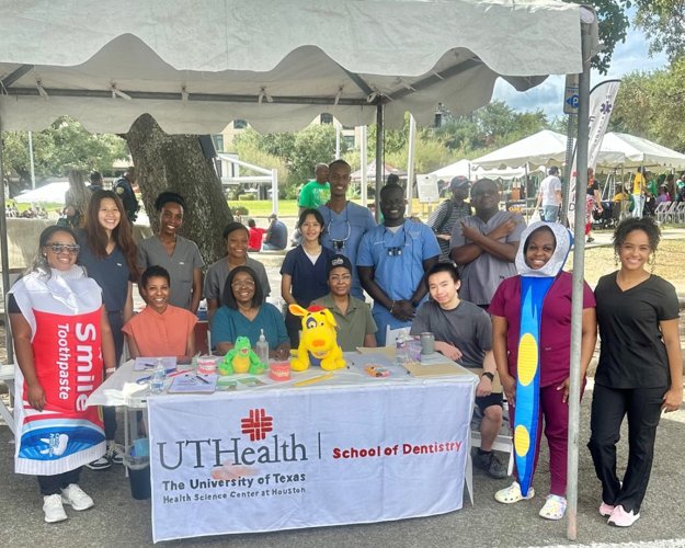 Group of people seated and standing behind a table under a canopy at an outdoor event.