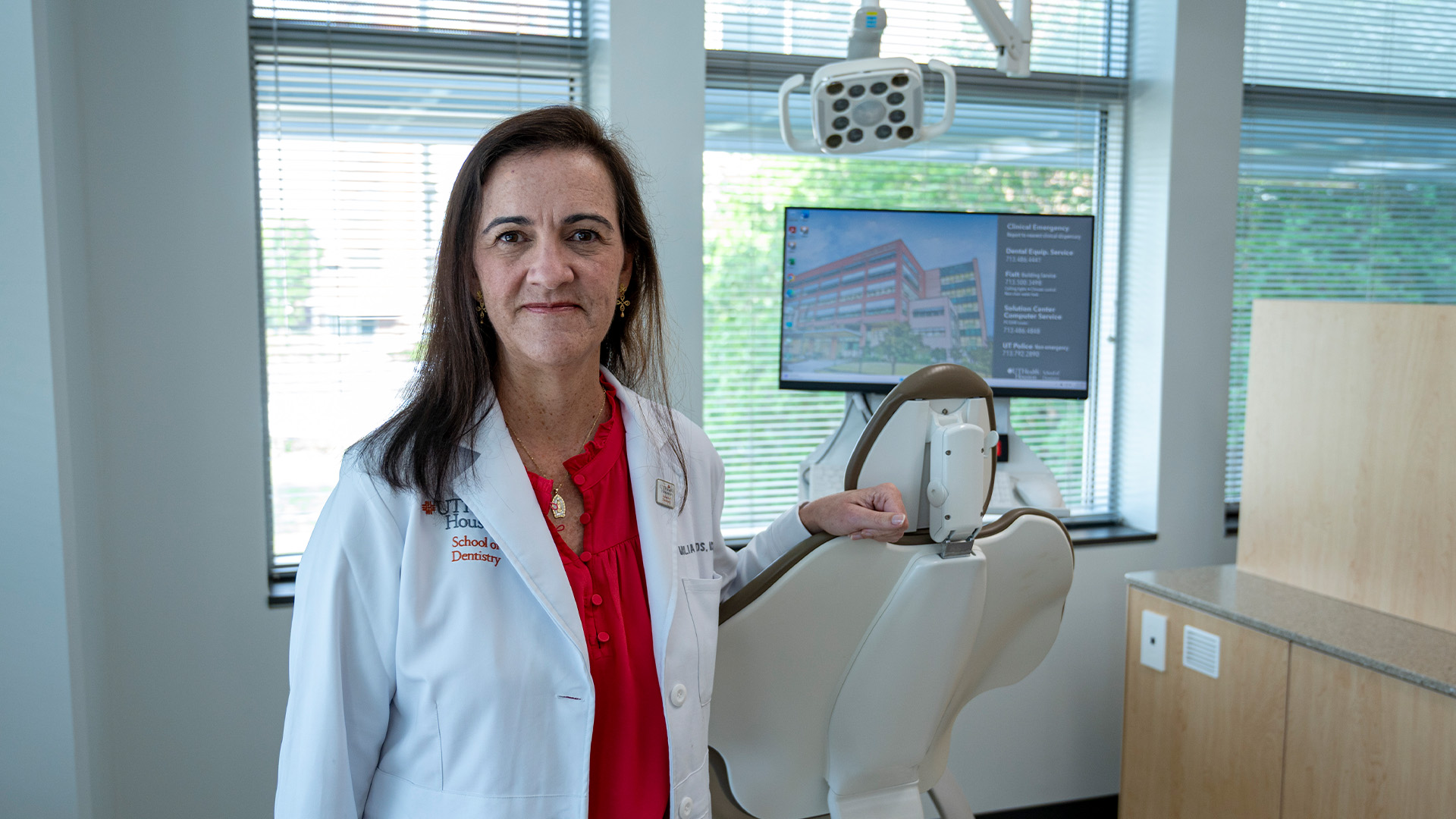 A person in a white lab coat stands beside a dental chair.