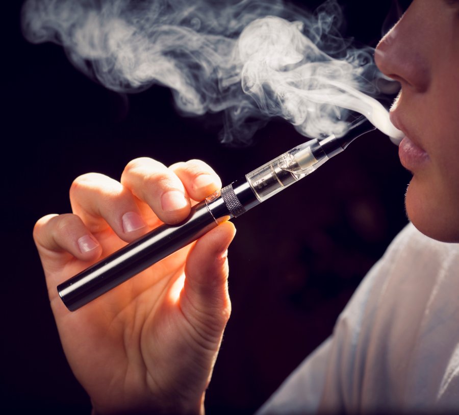 A young man holding an e-cigarette exhales vapor.