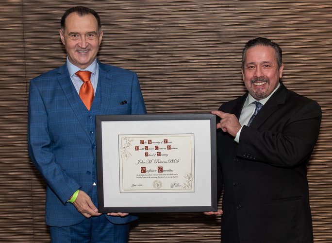 Drs. Rade Paravina and Joe Ontiveros pose for a photo with Dr. John Powers' framed professor emeritus certificate.
