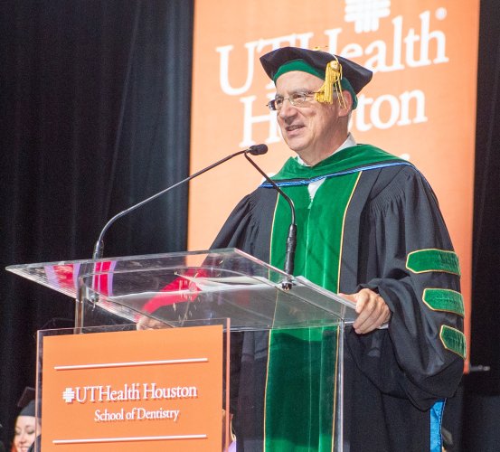 Man in regalia speaks at a podium during commencement.