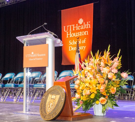 Flowers displayed in front of a podium and chairs on a stage.