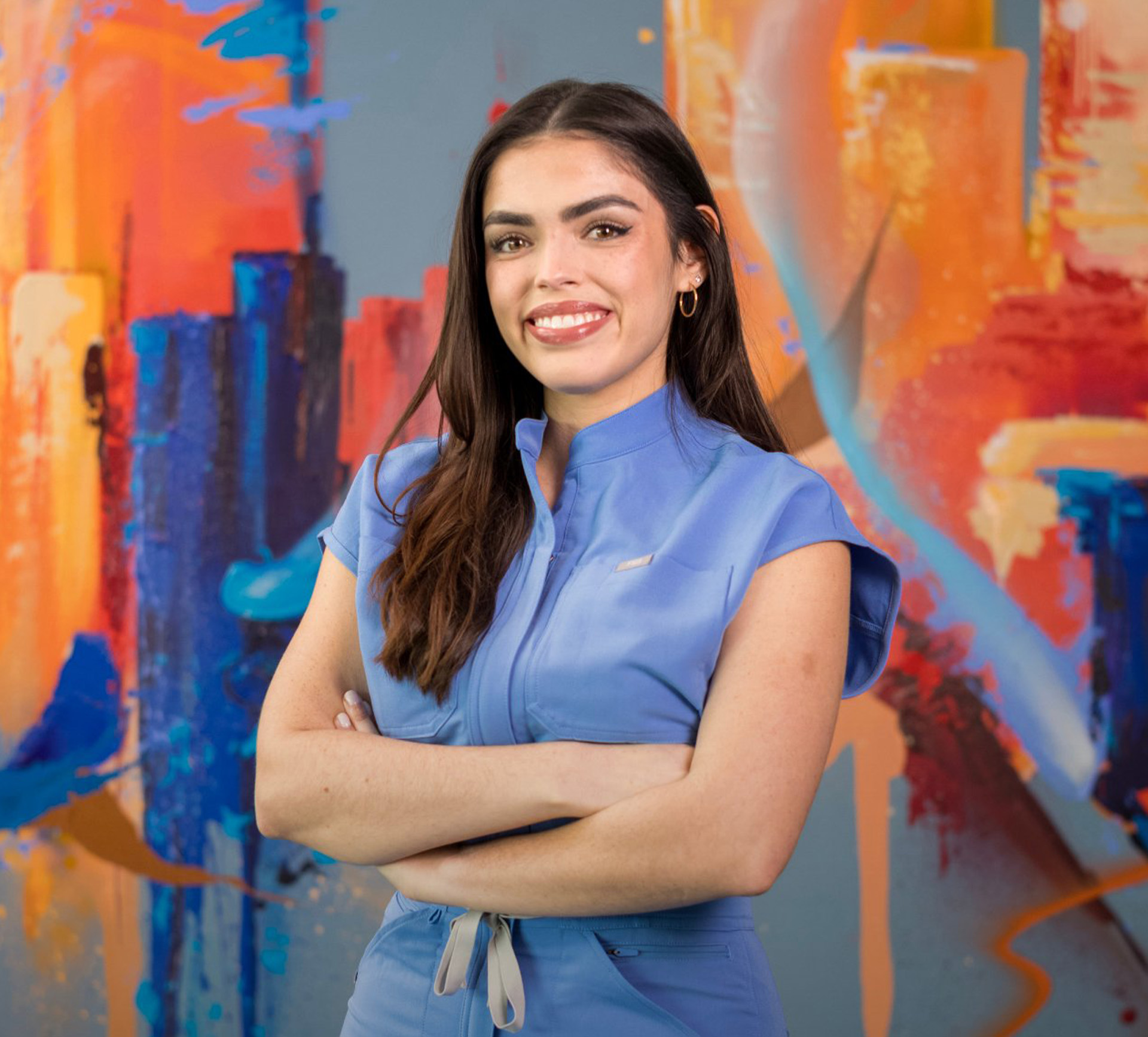 Female dental student in blue scrubs stands with arms crossed in front of a painted mural of the Houston skyline.