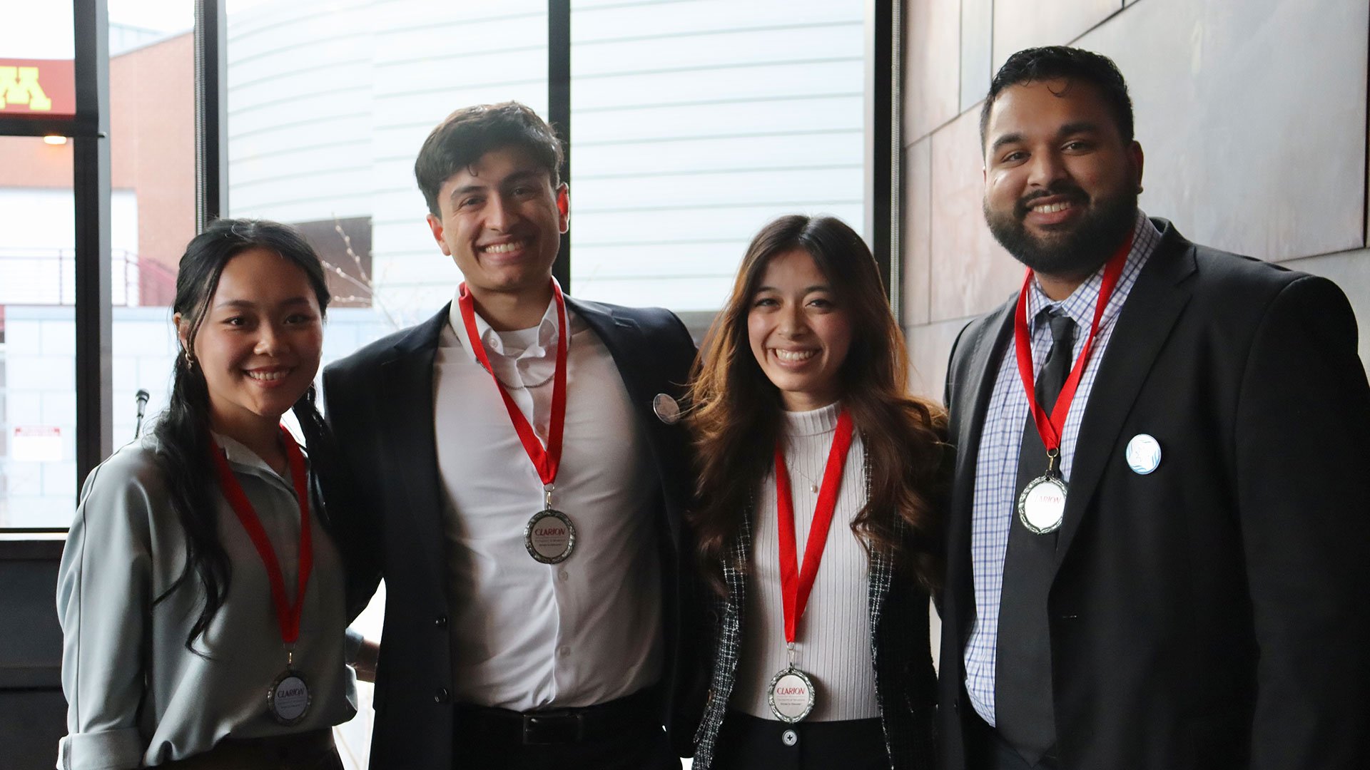 Four people wearing medals with red ribbons stand together in front of a window.