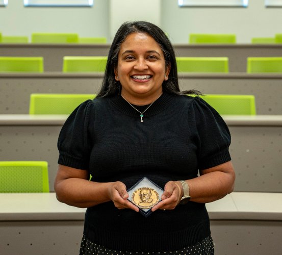 Person holding an award in an empty lecture hall with green seats.