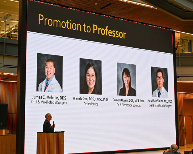Person presenting from a podium in front of a large video board.