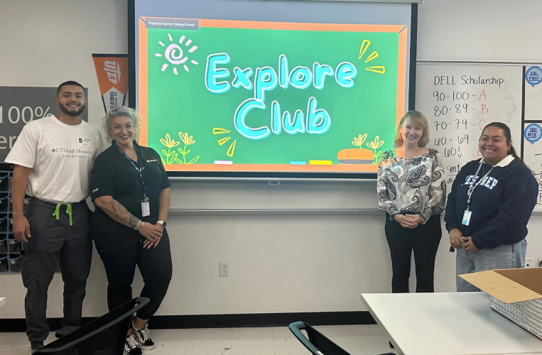 Four individuals gather around a projector screen inside a classroom.