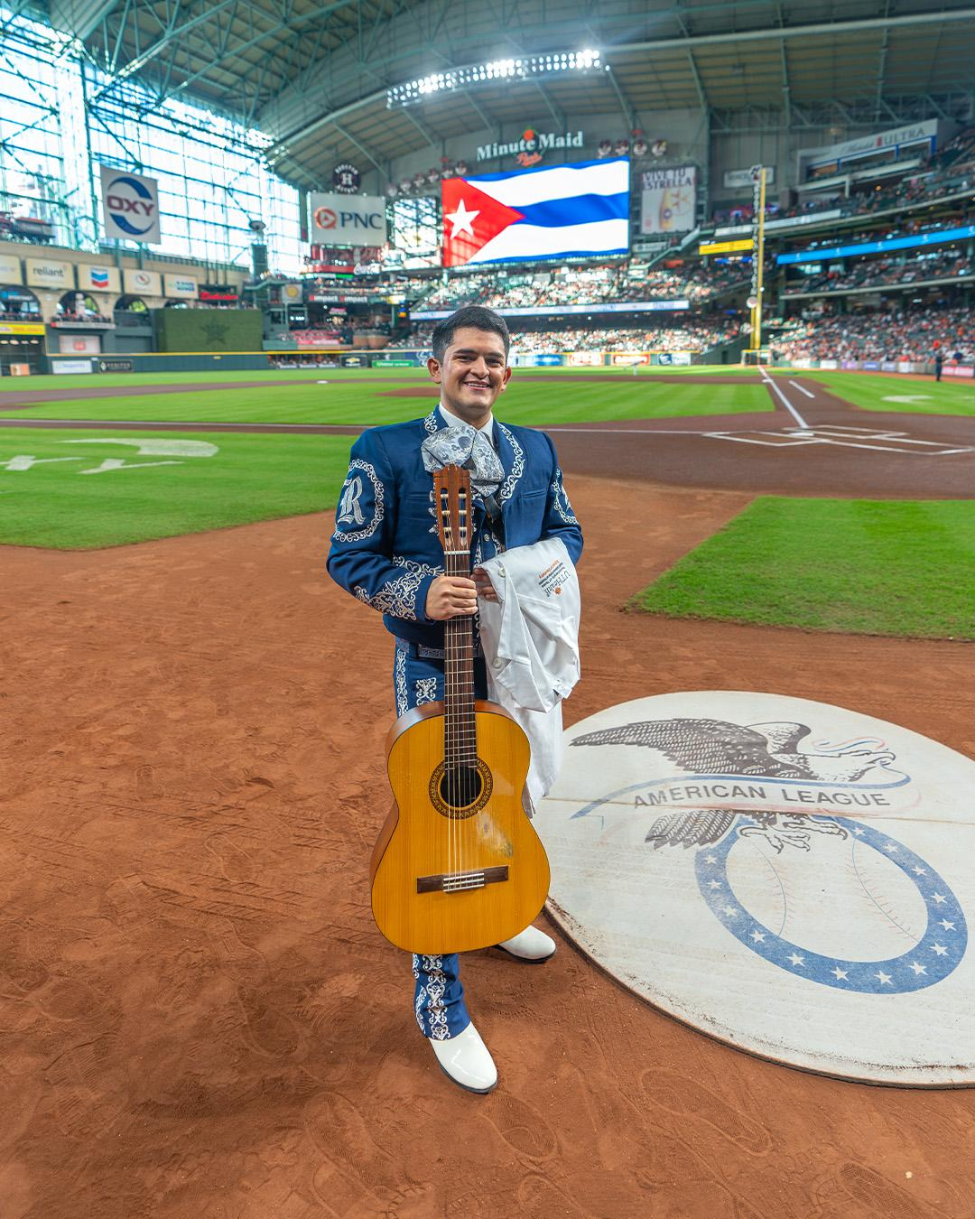 Dental student Cesar Zapata behind home plate with his UTHealth Houston School of Dentistry white coat ahead of his national anthem performance with his mariachi band, Mariachi Luna Llena.