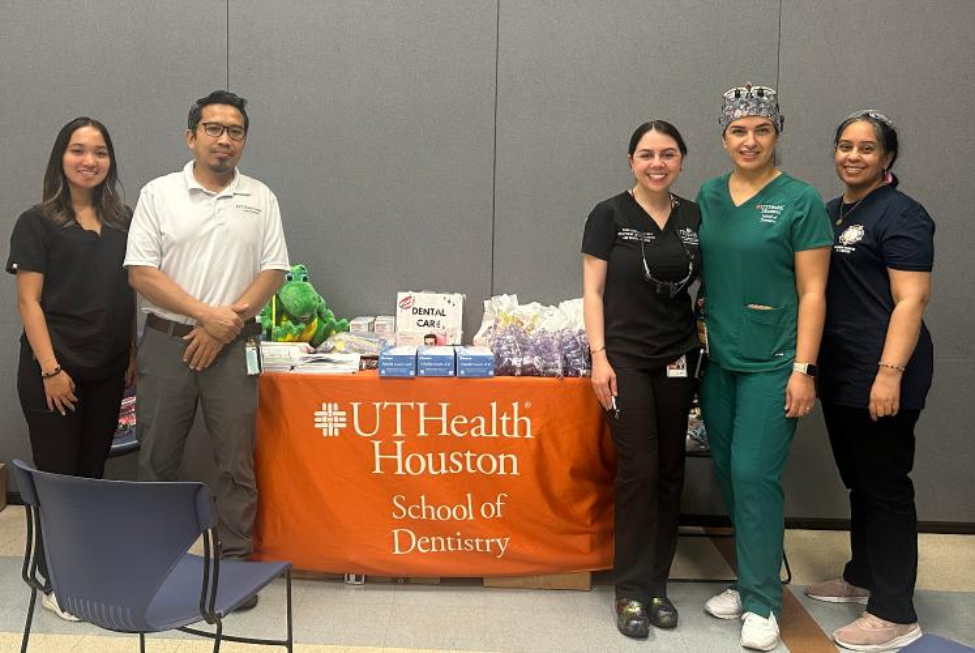 Several people stand in front of a table topped with dental supplies and helpful information.