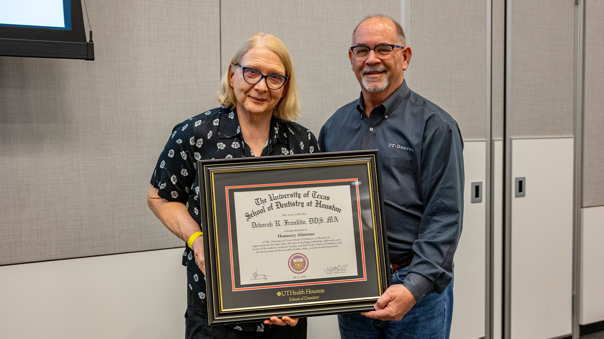 A pair of individuals stand indoors holding a framed UTHealth Houston School of Dentistry certificate recognizing Deborah R. Franklin as an Honorary Alumnus.