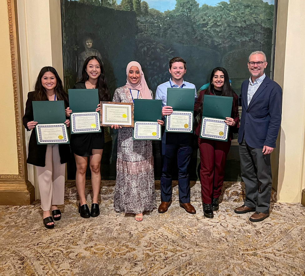 Group photo of five dental students holding certificates with a faculty member.