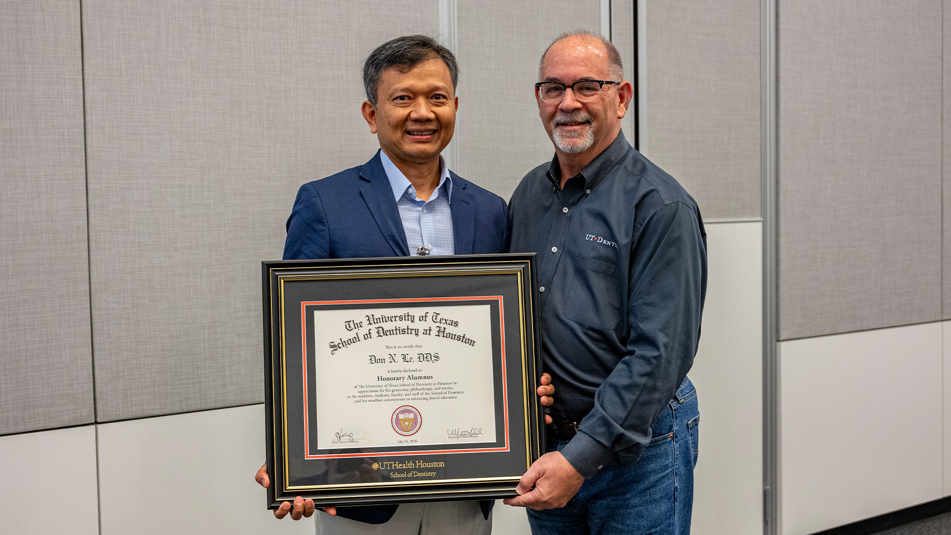 Two individuals stand indoors holding a framed UTHealth Houston School of Dentistry certificate recognizing Don N. Le as an Honorary Alumnus.