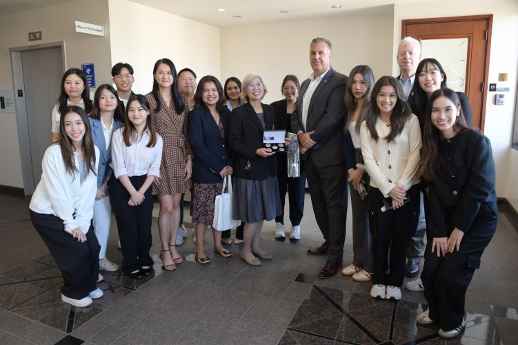 Group of people in professional business attire, presenting a gift in a hallway.
