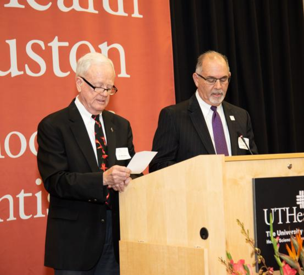 Two men, UTSD Alumni Association President Ron Collins, DDS ’79 (left), and Dean John A. Valenza, DDS ’81, stand at the podium reading The Dentists' Pledge from program insert.