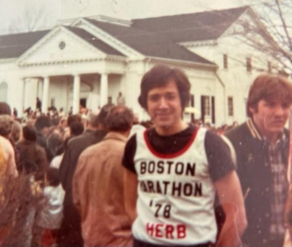 Herbert Dorris, DMD, pictured wearing a Boston Marathon shirt in front of a white house.