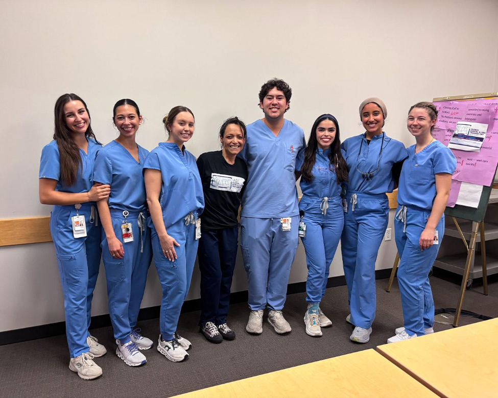 Students in light blue scrubs stand with a faculty member wearing a black shirt that features the Global Dental and Oral Trauma Day logo.