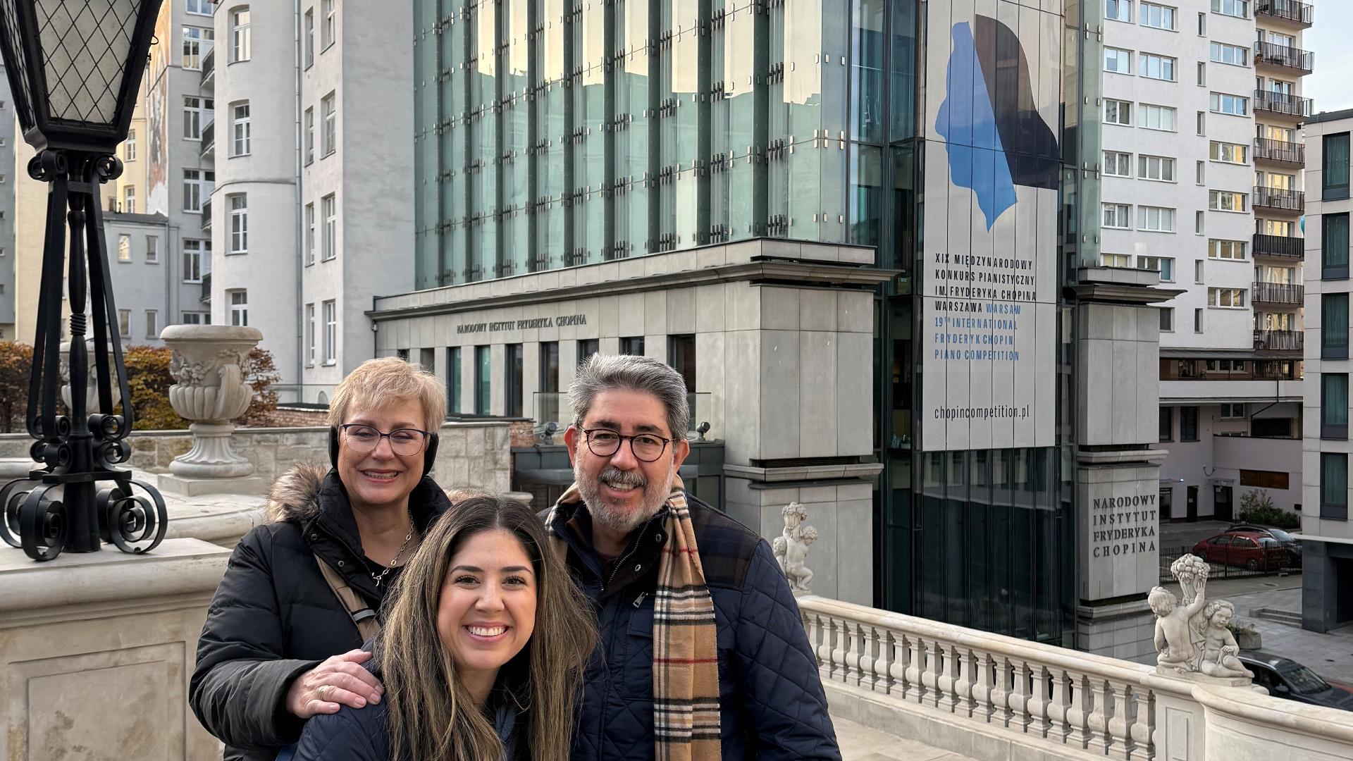 Husband and wife stand behind their daughter dressed in warm clothing for a group photo in front of the Museum of Fryderyk Chopin in Warsaw, Poland.
