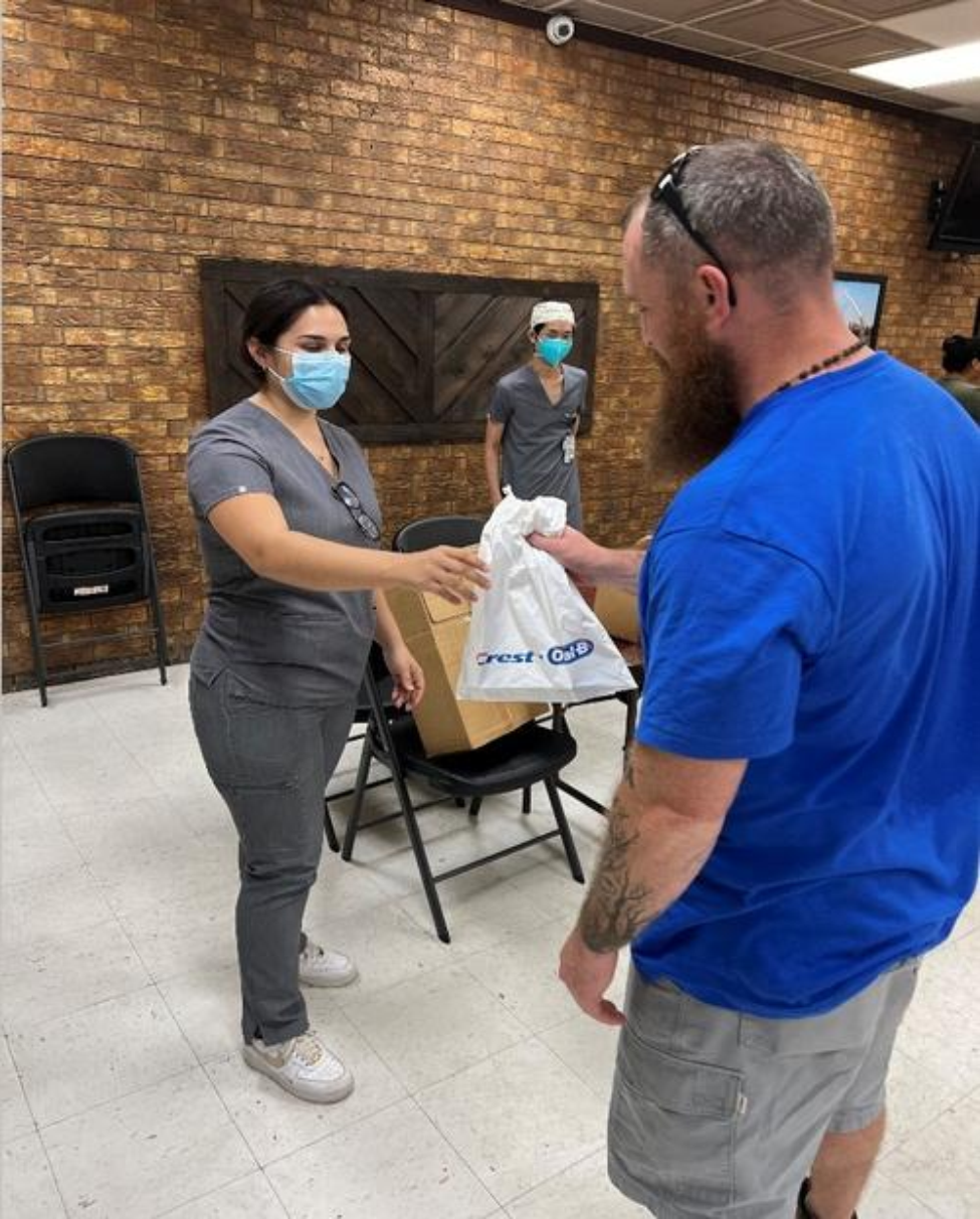 Dental students Elissa Guerra (left) hands a oral hygiene goodie bag to “Community Back to School” participant.