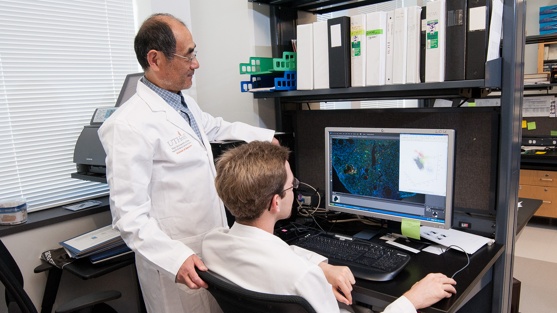 Two dentists gathered around a computer screen, doing research.