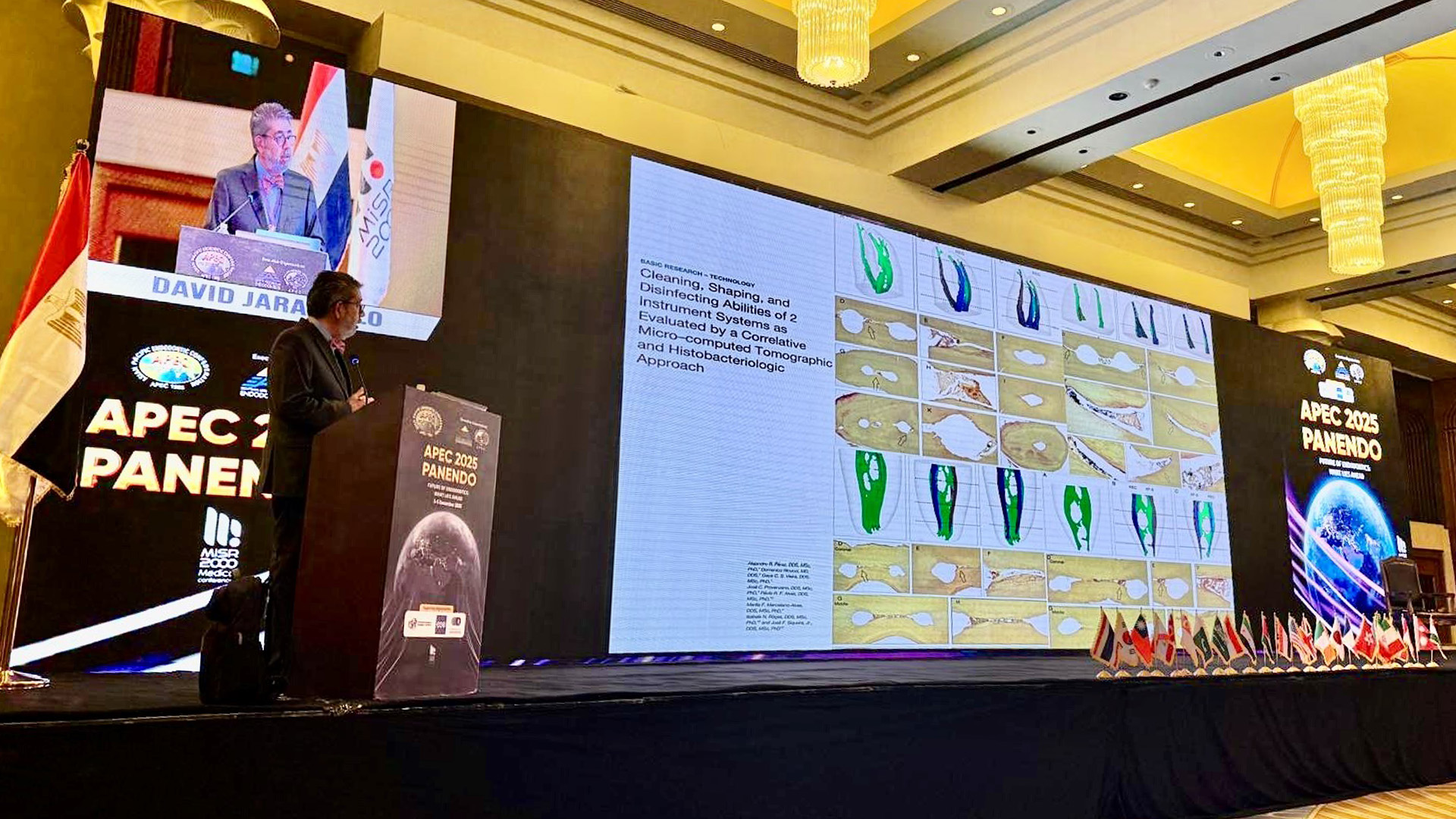 Man speaks on stage at a conference in front of a large digital screen.