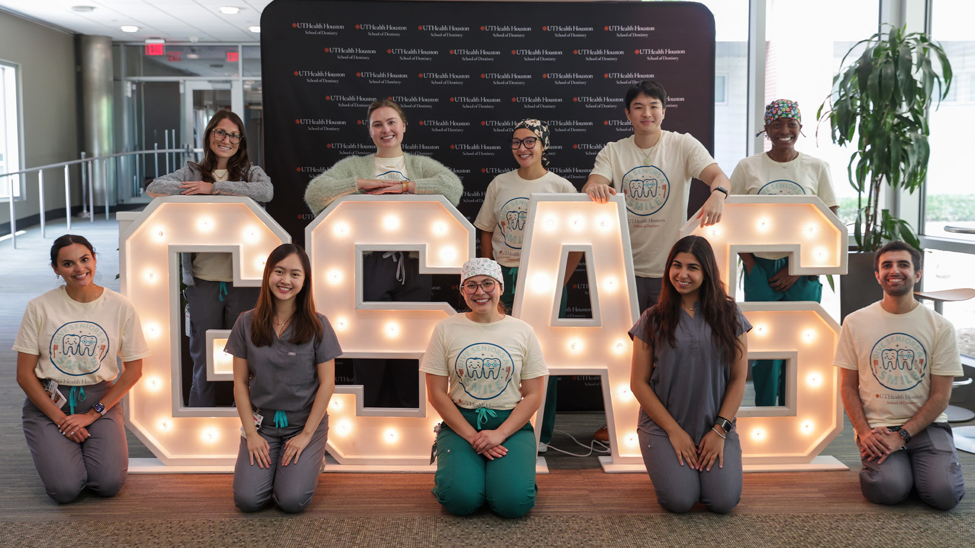 Ten people stand indoors in front of illuminated 